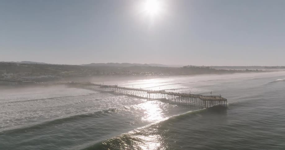 Aerial panorama of a pier reaching the sea on a beach with the sun on the horizon