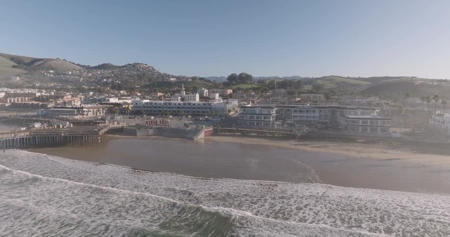 Aerial view of a beach with a long pier and an urban city in the background
