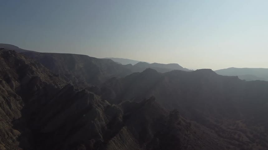 A vast mountain range stretches across the frame under a clear sky with the rocky terrain fading into a hazy distance
