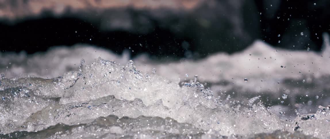 Water splashes and churns in slow motion as it flows downstream creating white water and spray in a closeup view