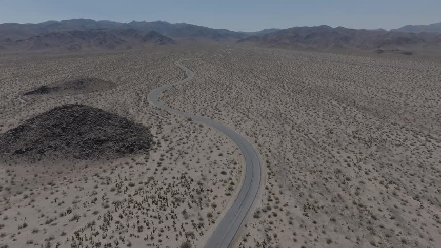 Aerial view of a highway winding through an arid region with mountains in the background