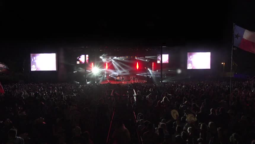 The singer is playing on stage in front of a large group of men and women and the lights are going everywhere flashing and lighting up the area