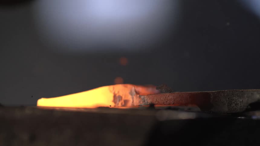 Close up of a hammer hitting a hot forge iron