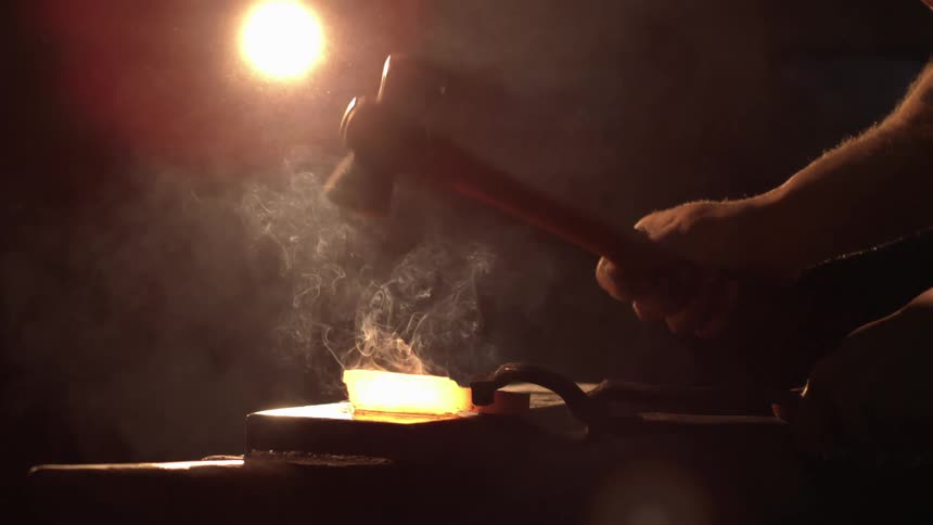 A man uses a hammer to hit a piece of hot metal