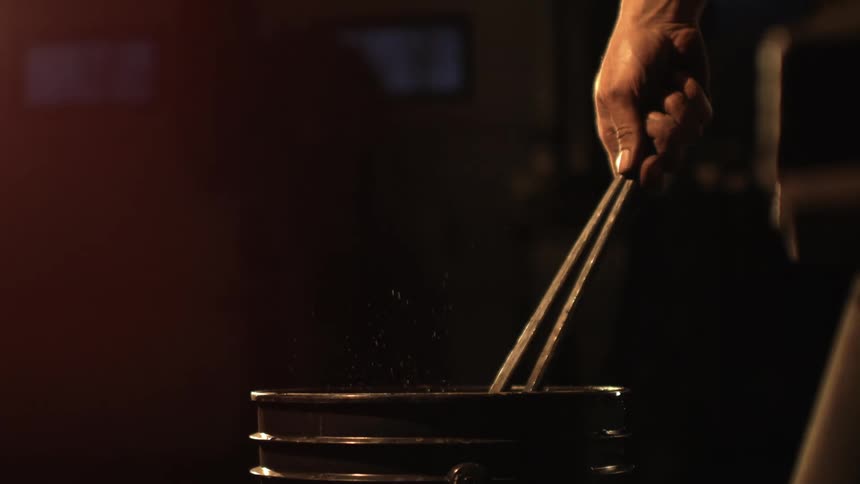 A blacksmith plunges hot metal tongs into a bucket of water creating steam and sparks
