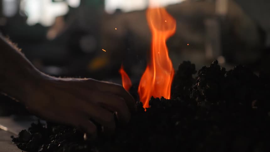 Pair of hands interacting with coals next to a lit fire