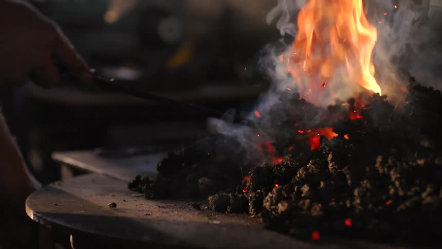 Man stoking fire with an iron instrument