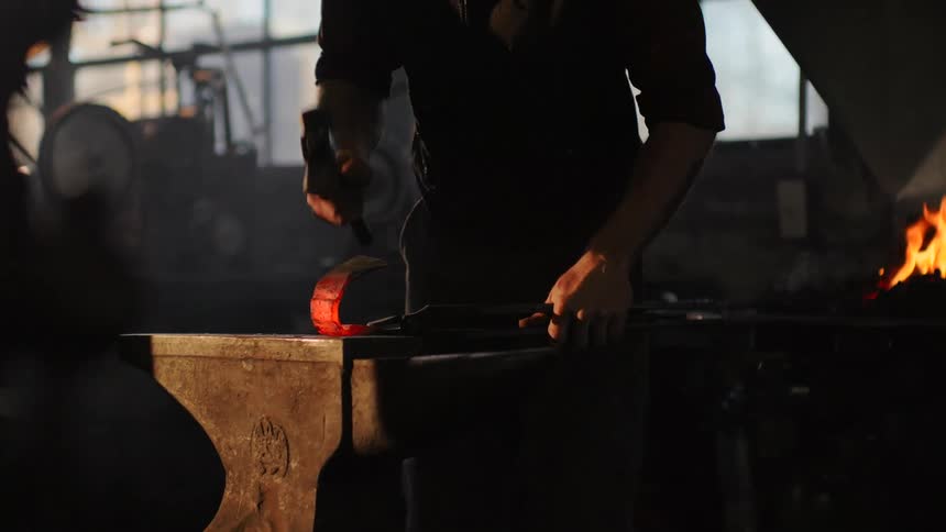 A man is hammering red hot metal on an anvil