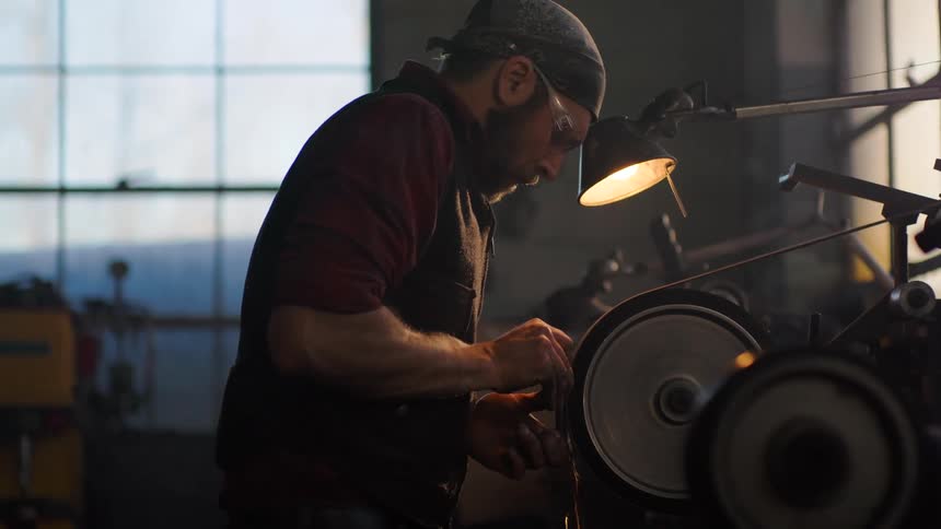 Man uses a power tool to polish a metal part in a workshop environment