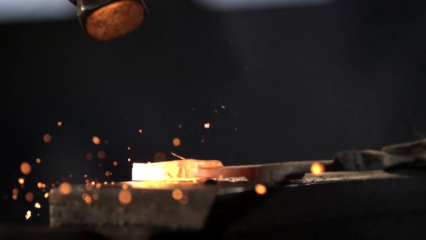 Sparks fly as a man hits hot metal with a hammer