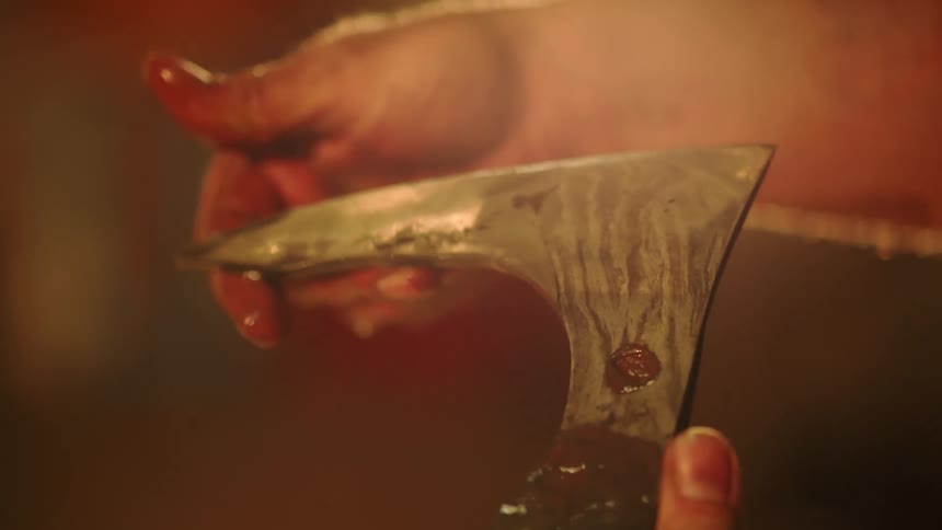 A closeup shows a blacksmiths hand carefully inspecting the blade of an axe head