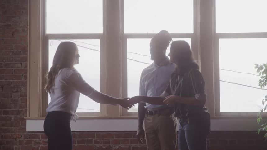 A woman shakes hands with a couple in a house
