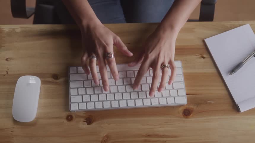 A womans hands typing on a white wireless keyboard with a writing pad and mouse beside her