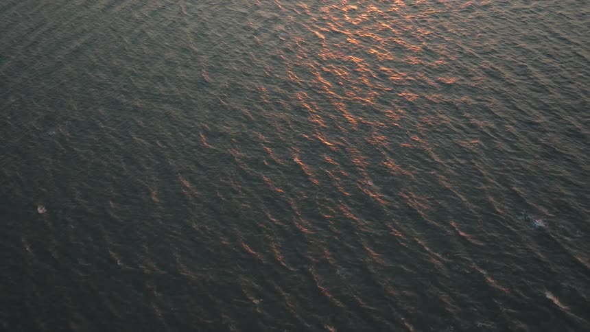 An aerial view looking down at the oceans surface showcasing textured waves and the shimmering reflection of sunlight on the water