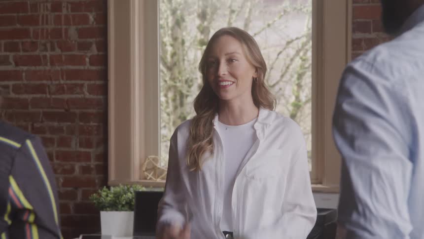 A woman is laughing while standing with her back to a window and talking with two friends