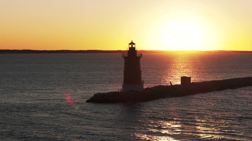 Small waves move past a jetty with a lighthouse on it