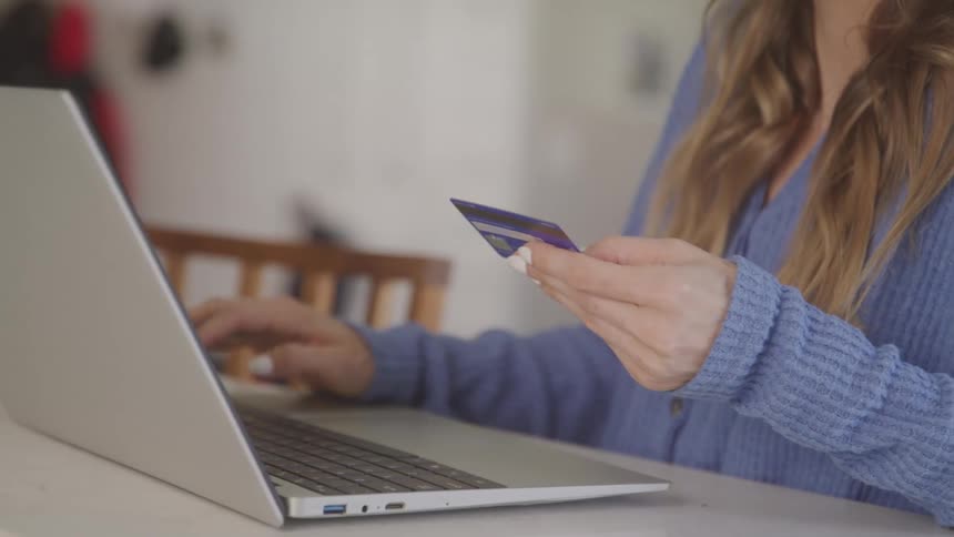 Woman with long hair types credit card information into a laptop