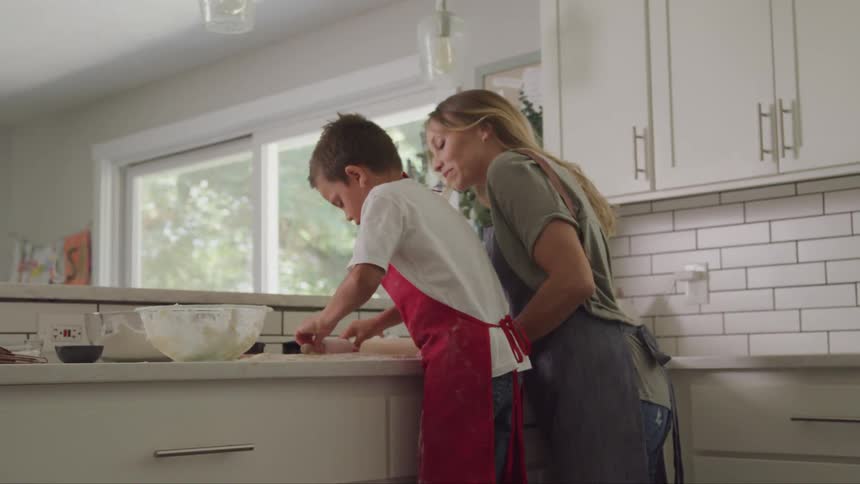 Boy and a woman both wearing aprons prepare something together in the kitchen
