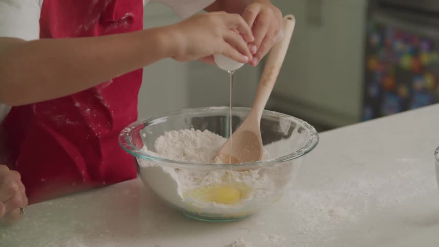Cracking egg and letting yolk and whites fall into flour in glass mixing bowl