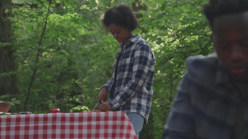Man and woman prepare a meal while outdoors near the woods