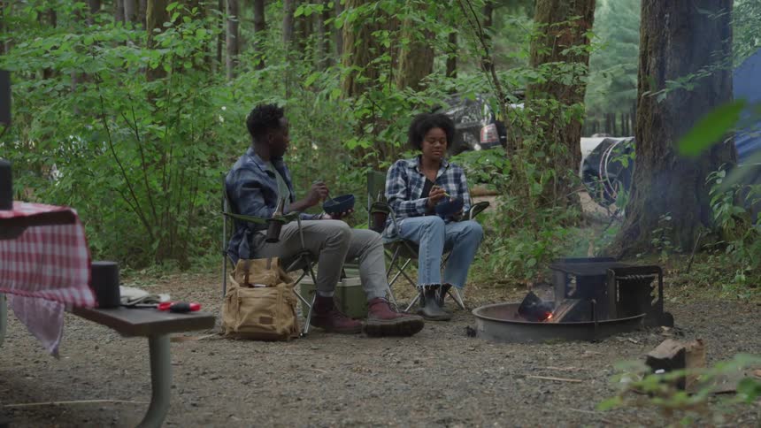 2 boys eating and talking while sitting in a field in the woods