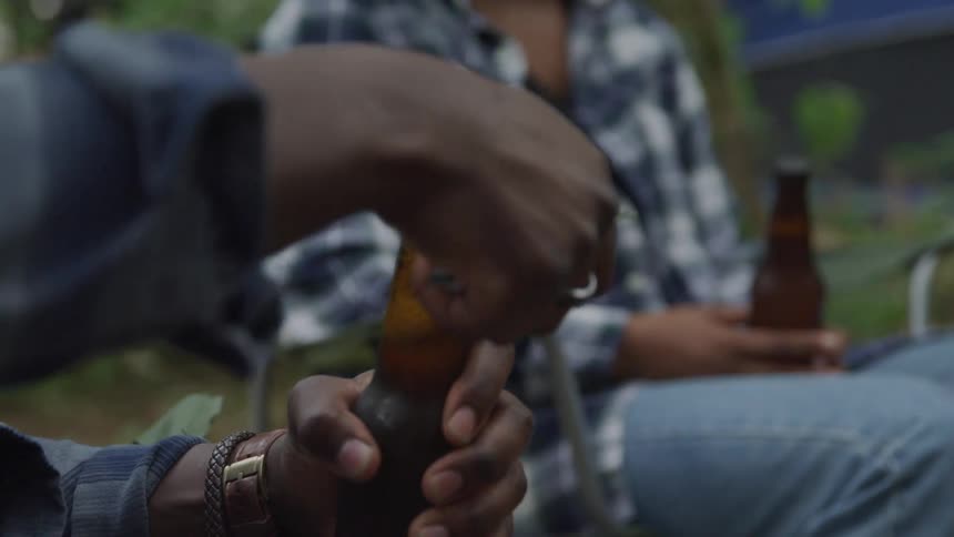 A man opens his beer bottle while camping