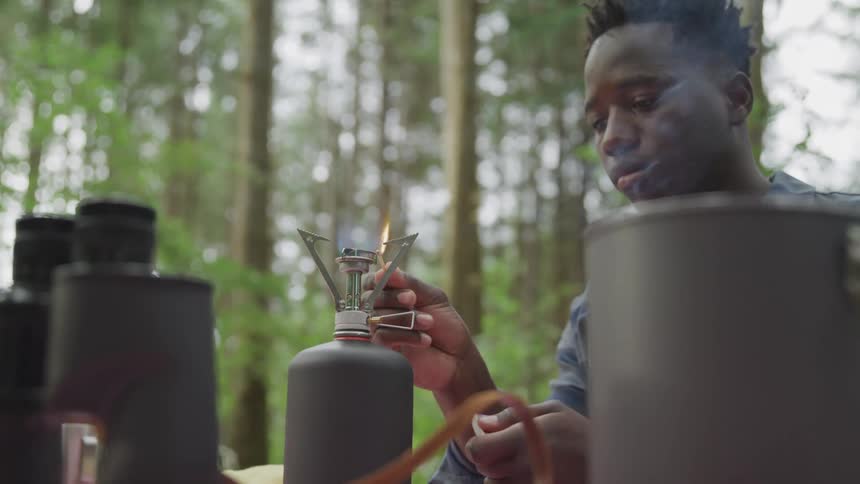 A man lights a mini propane grill while camping