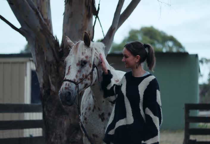 A teenage girls smiles as she rubs her horses neck
