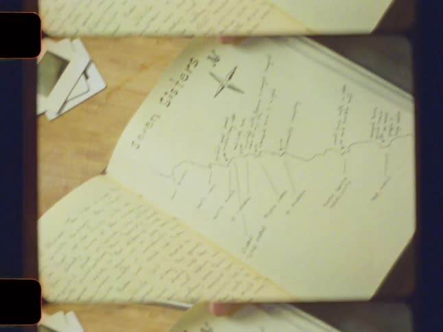 A hand flips through the pages of an open notebook revealing a handdrawn map with labeled paths a compass rose and detailed annotations