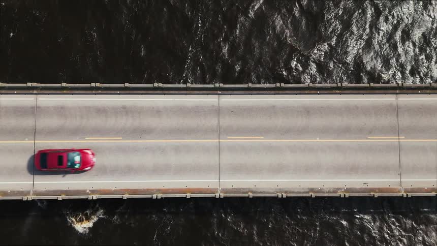 An aerial topdown view shows cars driving across a bridge spanning over a body of water