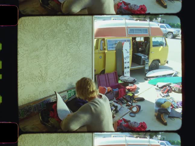 A man organizes bags and scattered items near a parked yellow van on a sunny day