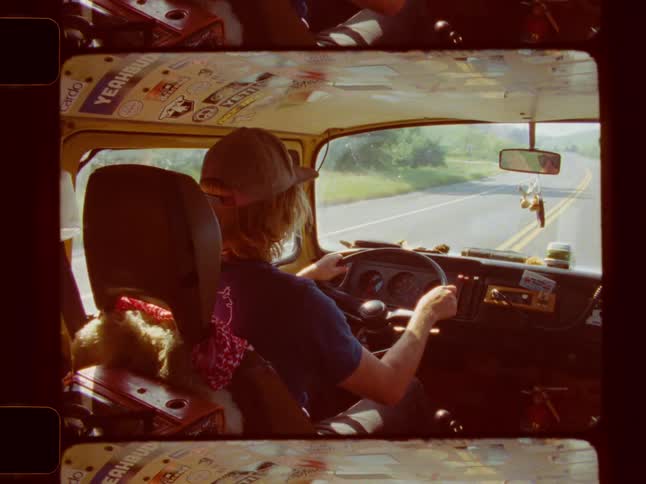 A person wearing a hat drives a vehicle with a cluttered dashboard looking out at a road ahead