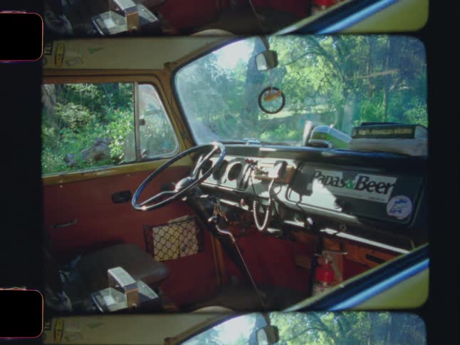 The interior of a vintage yellow van displays a dashboard with a cb radio framed by a windshield revealing a sunny forest day