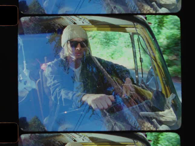 Young man wearing sunglasses and a beanie driving a van seen from outside through the windshield in a forested area