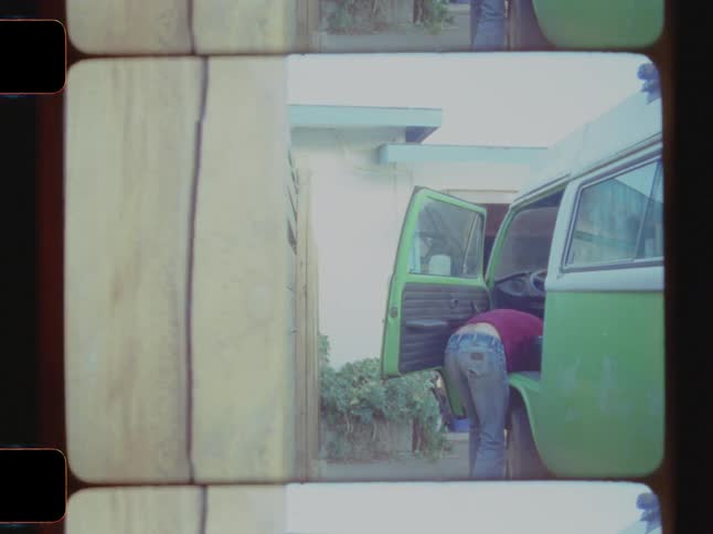 A man leans into the interior of a green van parked beside a house with half of his body inside