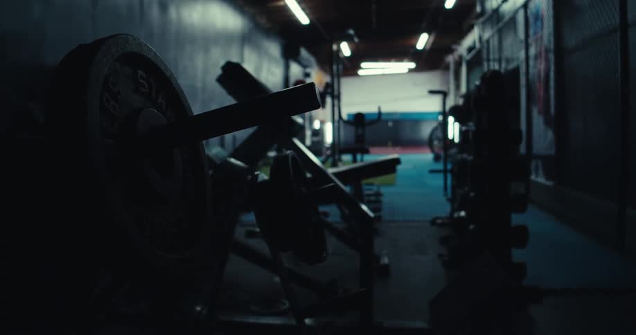 An initially illuminated gym with rows of weightlifting equipment and a hallway is plunged into darkness as the overhead lights are switched off