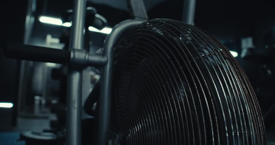 A closeup captures the spinning wheel of a stationary exercise bike in a gym its pedal moving although no one is visibly using it