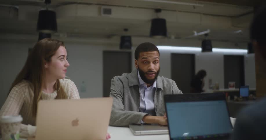Workers are talking with their laptops open at a meeting