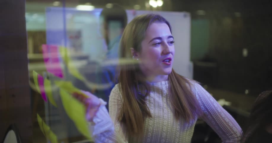 Girls talking to each other in front of a whiteboard with postit notes and reasoning together