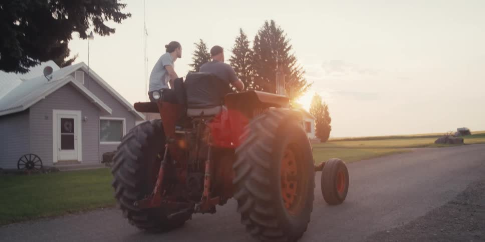 Two men are riding on a tractor at sunrise