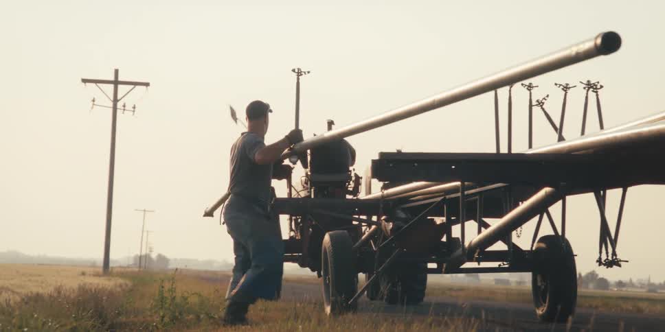 A man loads a long pipe on a tractor