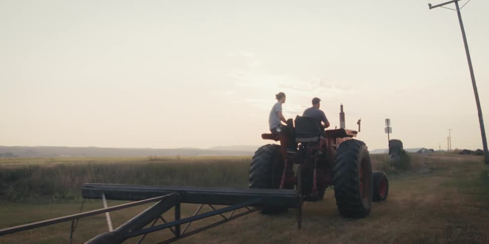 2 men ride a tractor in the fields