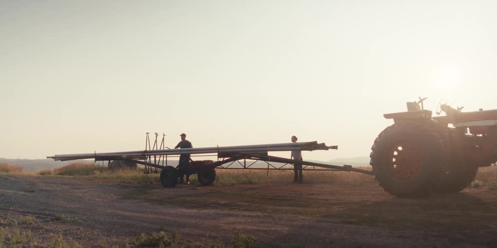 Two farmers put a long pipe on the trailer