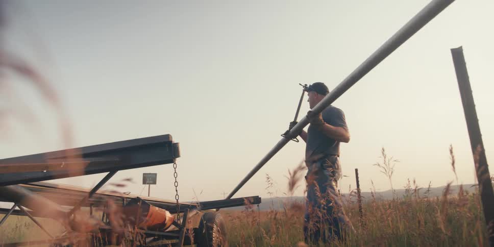 Man working in a field with long aluminum pipes