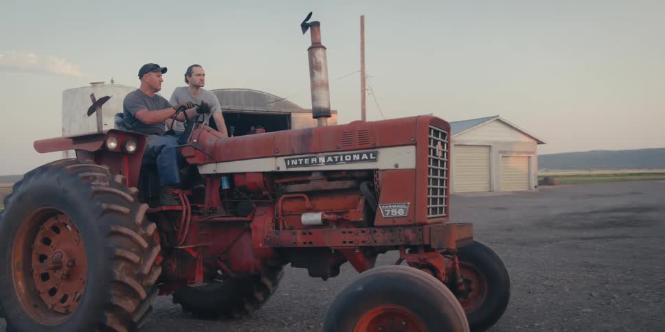 Two men ride on a tractor on a farm