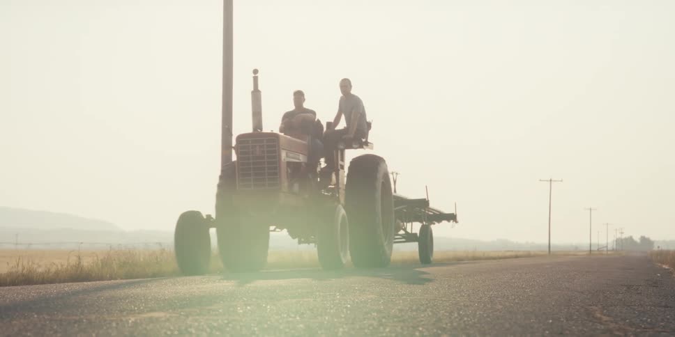 Two men on top of a tractor crossing the road