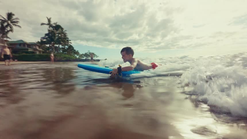 The little boy is riding the boogie board in on the waves