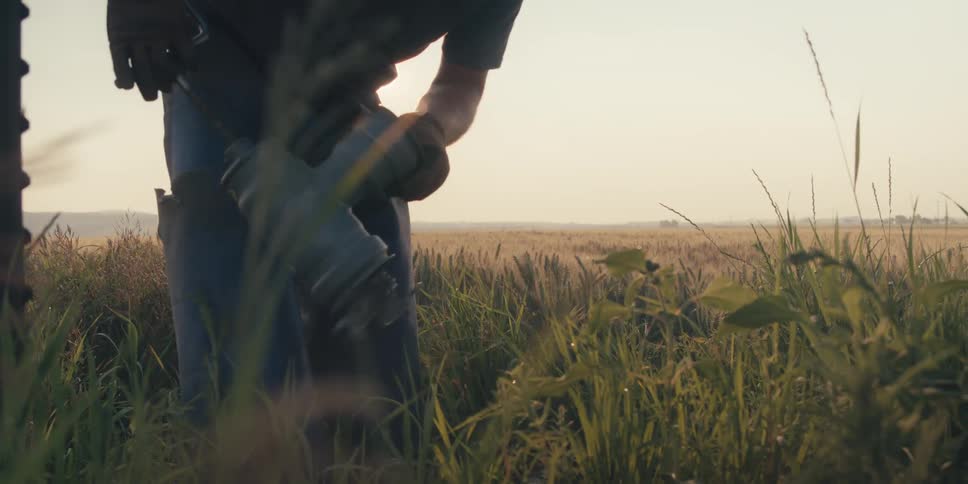 Man in the middle of a field picking up a tool to work