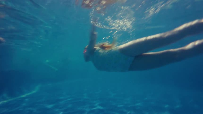 A girl is swimming underwater in the pool