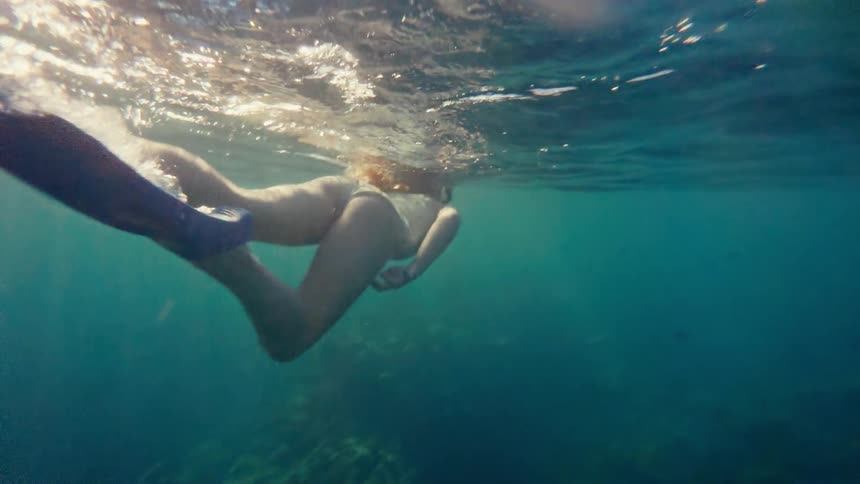 A woman is snorkeling underwater with bubbles and sunlight creating a dynamic watery scene